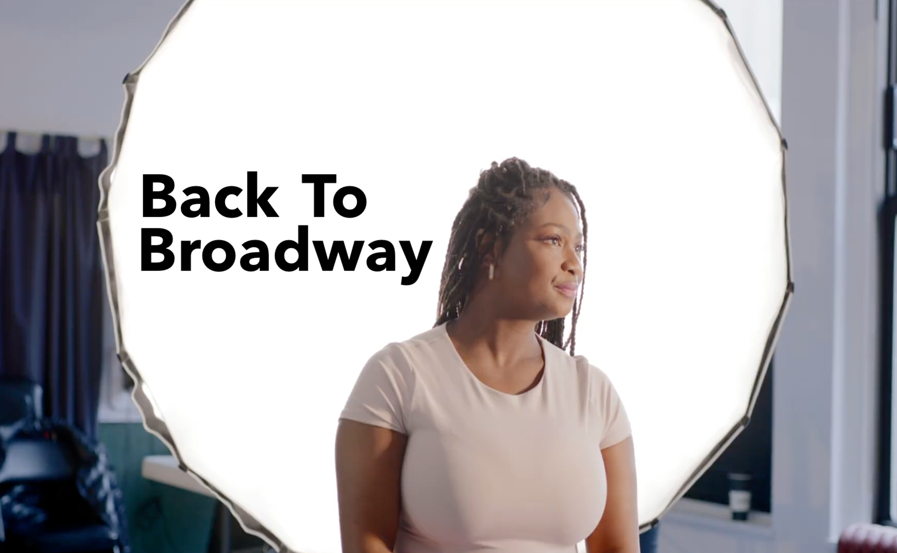 A woman with dreadlocks and earrings stands in front of a large, bright professional lighting setup. The text 'Back To Broadway' is overlaid on the image.