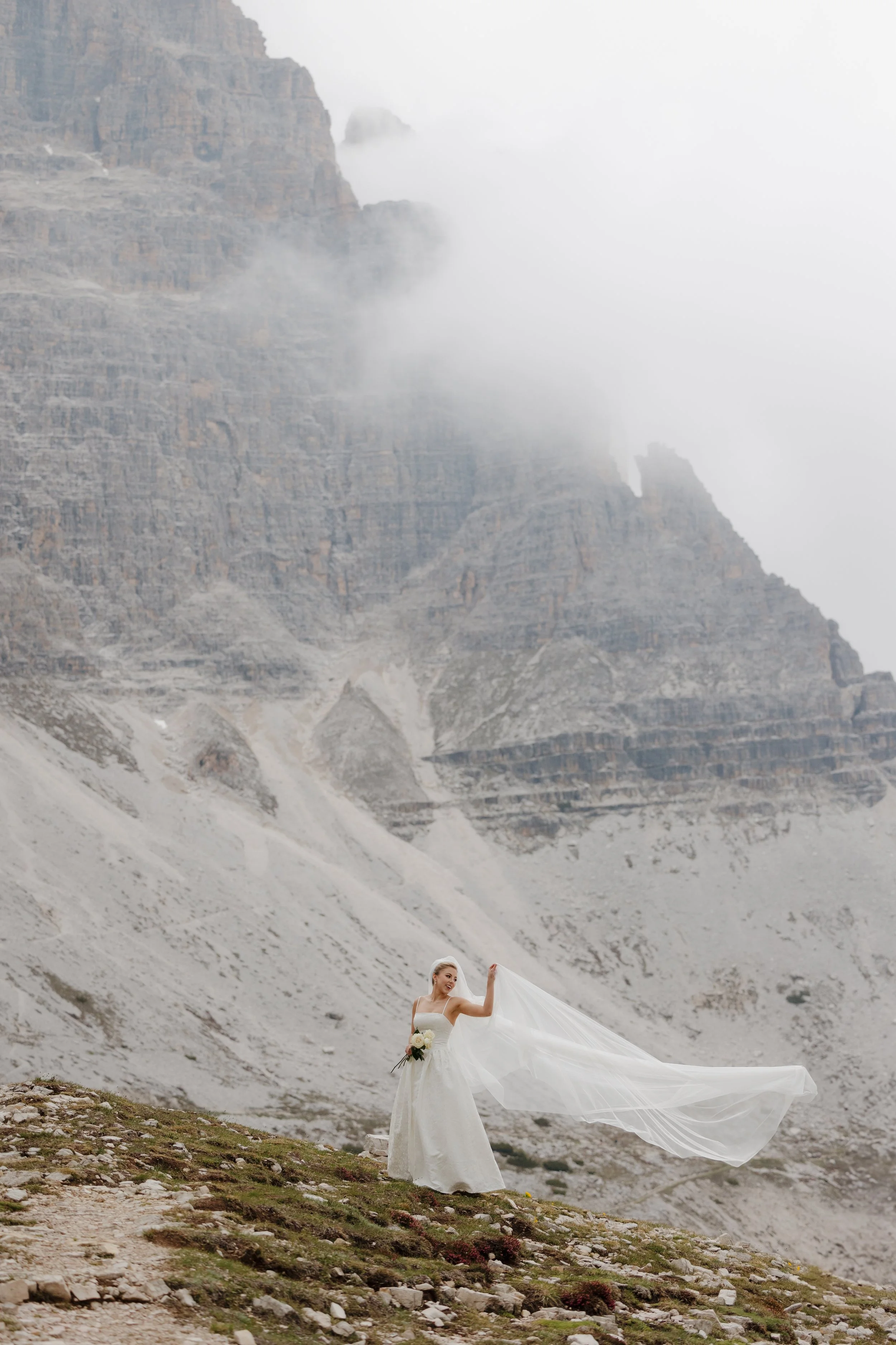 A bride tosses her long veil, standing in front of Tre Cime di Lavaredo in the Italian Dolomite.