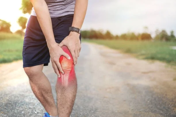 An athlete clutching their knee on a running path, representing runner's knee treatment and sports injury rehab at Indy Spine and Rehab in Carmel, Indiana.