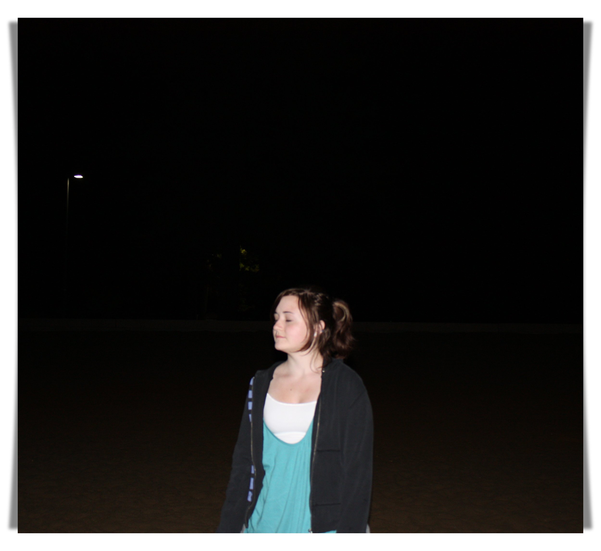 High school aged girl standing against dark background with eyes closed, at the time of disordered eating.