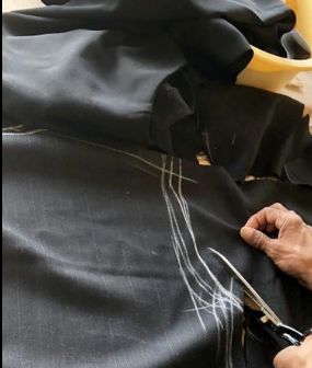 Tailor cutting black fabric with chalk markings - Sterling Fine Cleaning alterations and tailoring Los Angeles