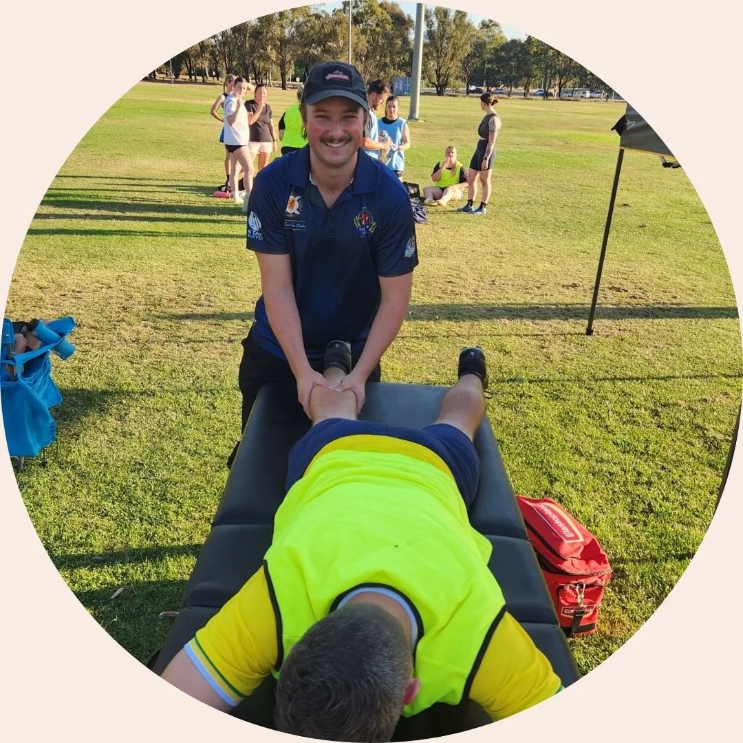 Photo of Jesse at a sports ground, massaging a soccer players calf.