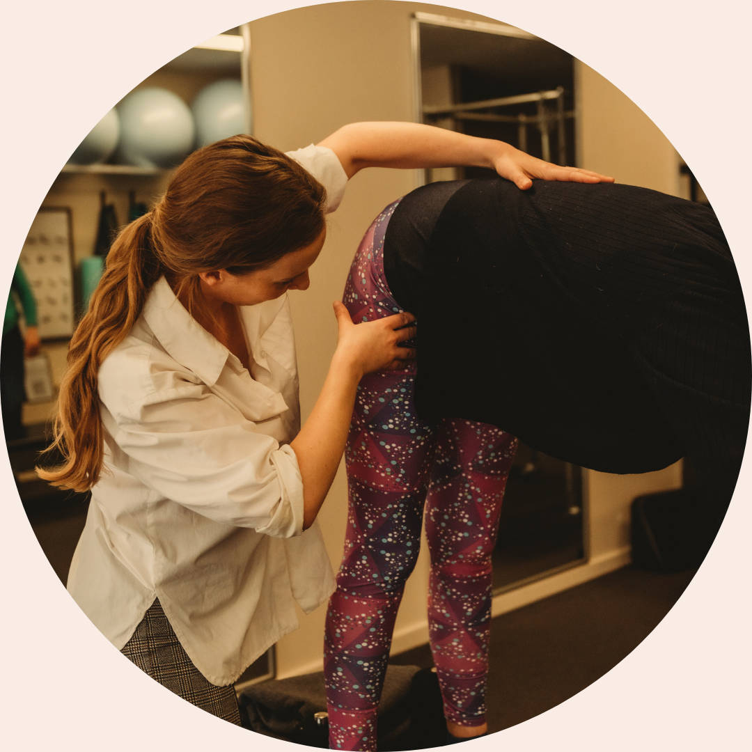 Physiotherapist assessing hip and lower back alignment during a movement assessment in a clinical pilates studio.
