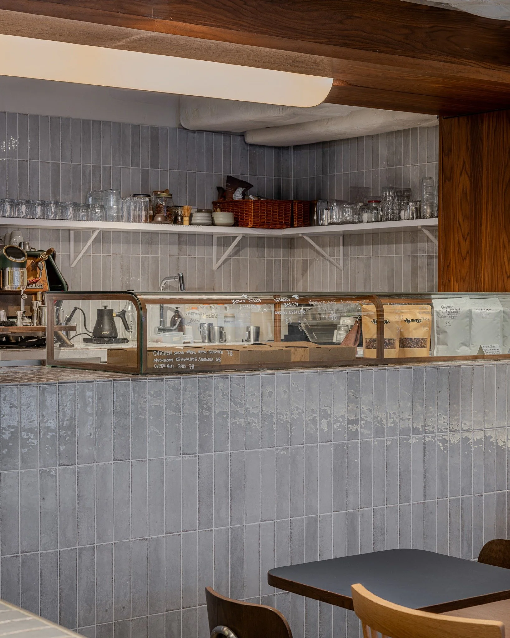 The artisanal hand-glazed tiles continue into the open kitchen&rsquo;s bespoke display case, showcasing an array of house-made Nordic pastries. A collection of bespoke lighting fixtures, from the facade sconce to the baguette-like fixture, transforms