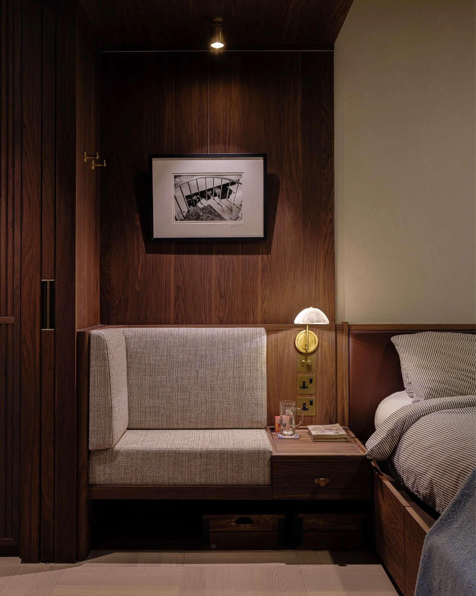 A serene ambiance embraces one once entered the bedroom. A grey fabric sofa extended from the headboard makes the perfect setting to read, illuminated by an alabaster bedside lamp. The fluted wardrobe doors with brass handles echo the overall narrati