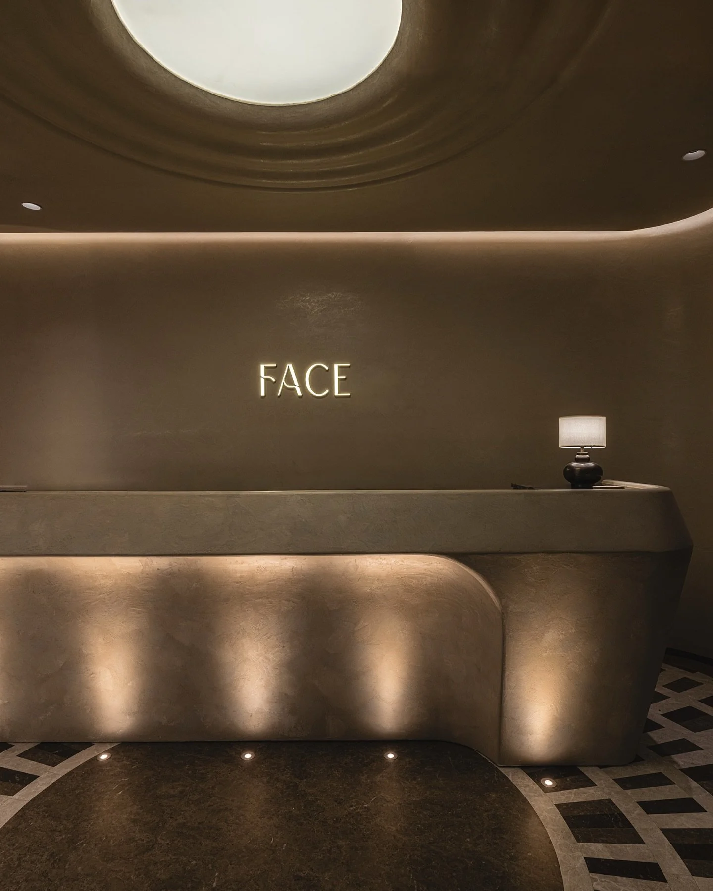 The reception area makes a striking impression. The radiant stone-patterned floor echoes the dimmable barrisol ceiling. Anchoring the space is an artisan-crafted sculptural island as the main reception. Uplights are precisely positioned to cast shado