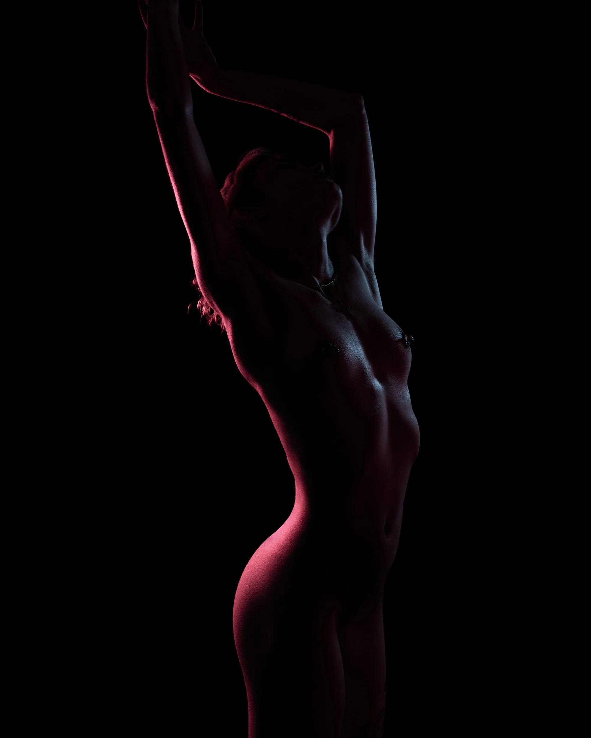 Silhouette of a woman with arms raised above her head, illuminated by pink lighting on a black background.