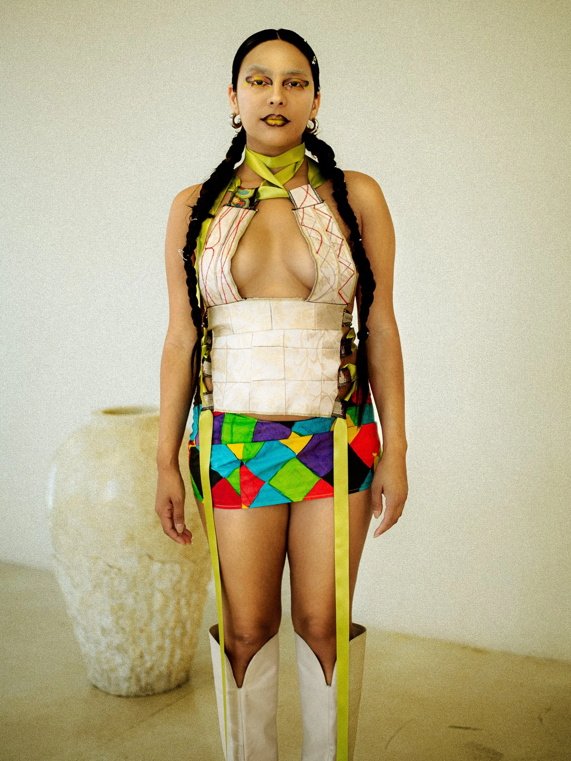 A tan woman model standing in front of a plain wall, dressed in colorful, eclectic clothing and makeup, photographed during a studio photography session in Los Angeles for a fashion editorial collaboration with fashion photographer Gí Tenamá