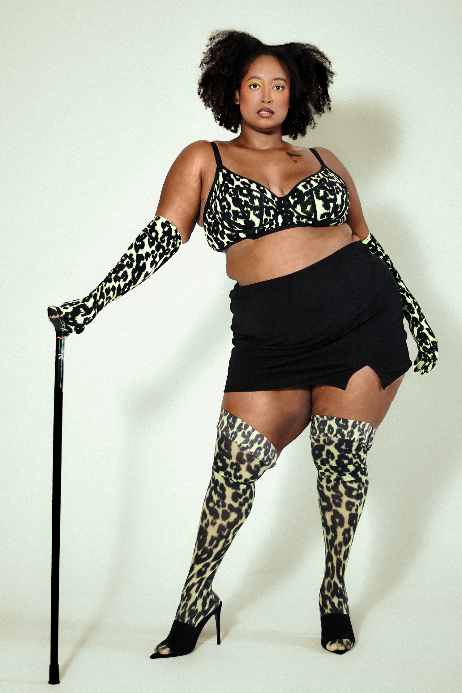 A Black woman holding her cane in cheetah print lingerie by Fenty x Fendi, Rihanna's brand, poses in a photography studio in Los Angeles, for a fashion editorial shoot directed by fashion editorial photographer Gí Tenamá "Gi Tenama"