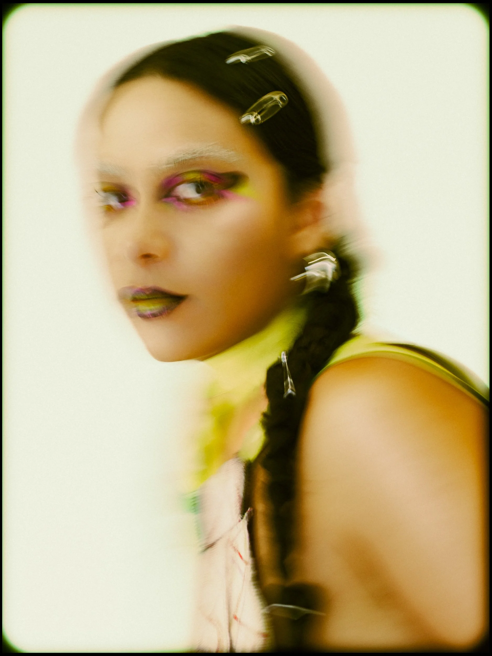 A woman model with colorful makeup and dark braided hair, blurred in motion against a light background, photographed during a fashion editorial photography session in Los Angeles with fashion photographer Gí Tenamá..