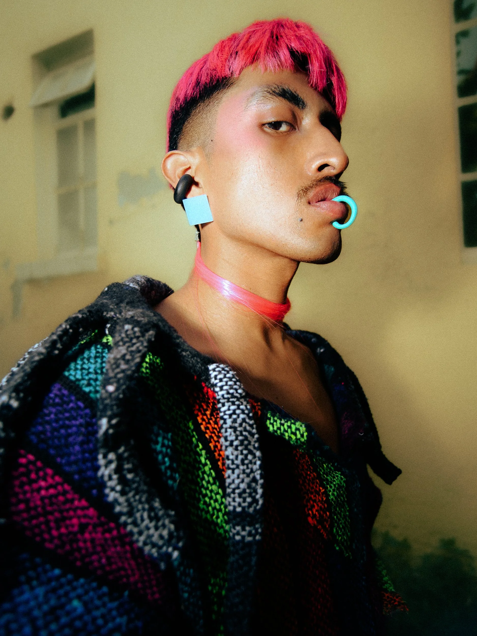 A feminine person model with pink hair, multiple facial piercings, and colorful clothing posing indoors, photographed during a fashion editorial photography session in Los Angeles with fashion photographer Gí Tenamá.