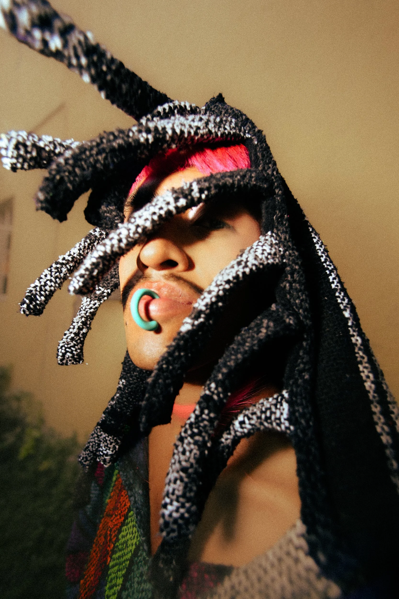 A feminine model with dreadlocks tied with black and white striped fabric, pink hair, a teal gauge in the ear, and wearing a colorful, patterned garment, photographed during a fashion editorial photography session in Los Angeles with fashion photogra