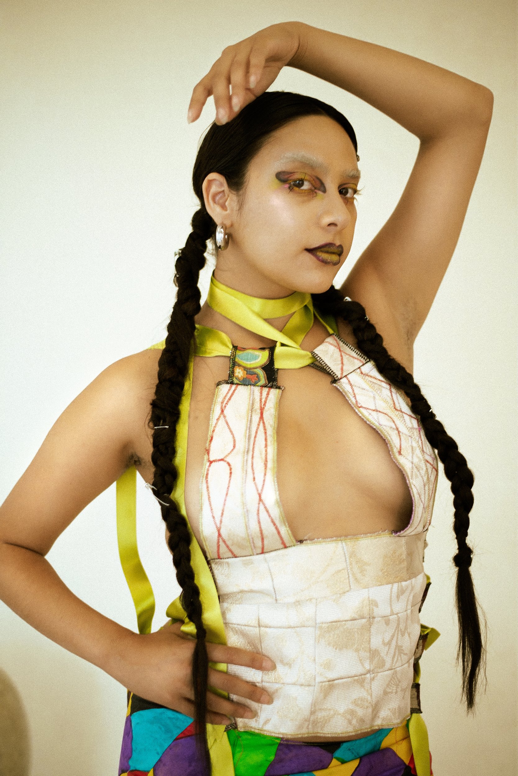 Person with long braided hair wearing colorful fashion, striking a pose with one hand behind head, against a neutral background, photographed during a fashion editorial photography session in Los Angeles with fashion photographer Gí Tenamá..