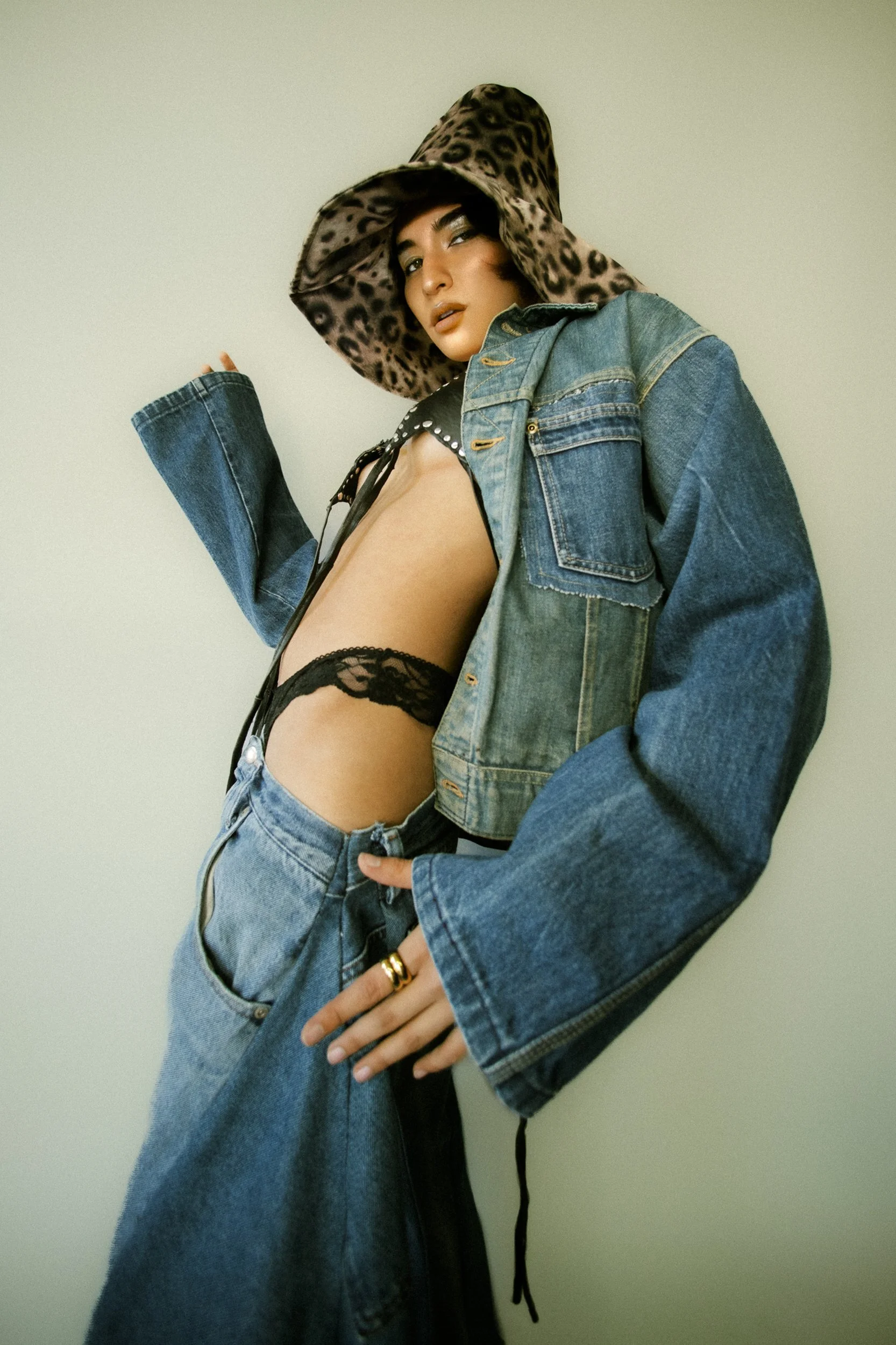 Model wearing a leopard print hood, denim jacket, black lace lingerie, and jeans, posing against a plain background, photographed during a fashion editorial photography session in Los Angeles with fashion photographer Gí Tenamá..