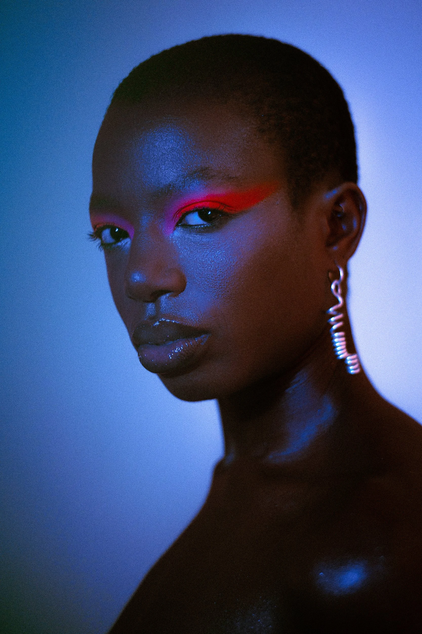 A portrait of a model with dark skin, short hair, colorful makeup, shiny lips, and an earring, illuminated by colorful lighting, A woman with curly black hair wearing bright makeup, earrings, a rainbow beaded bracelet, and a necklace with a large red