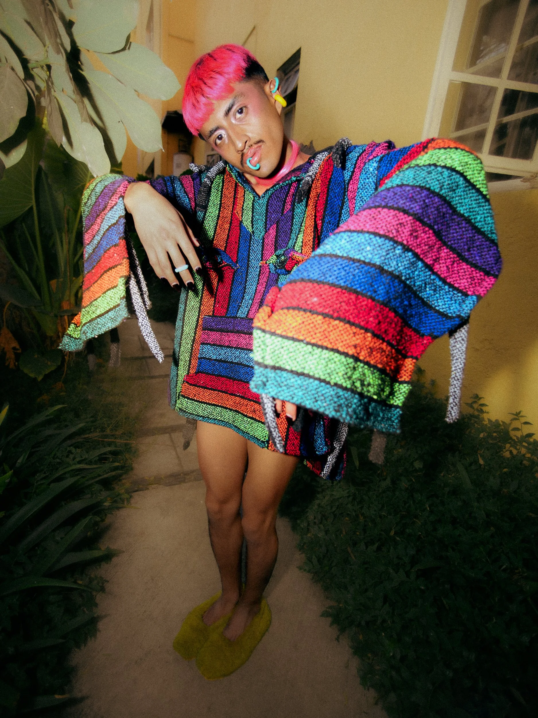A feminine person model with pink hair, multiple facial piercings, and colorful clothing posing indoors, photographed during a fashion editorial photography session in Los Angeles with fashion photographer Gí Tenamá.
