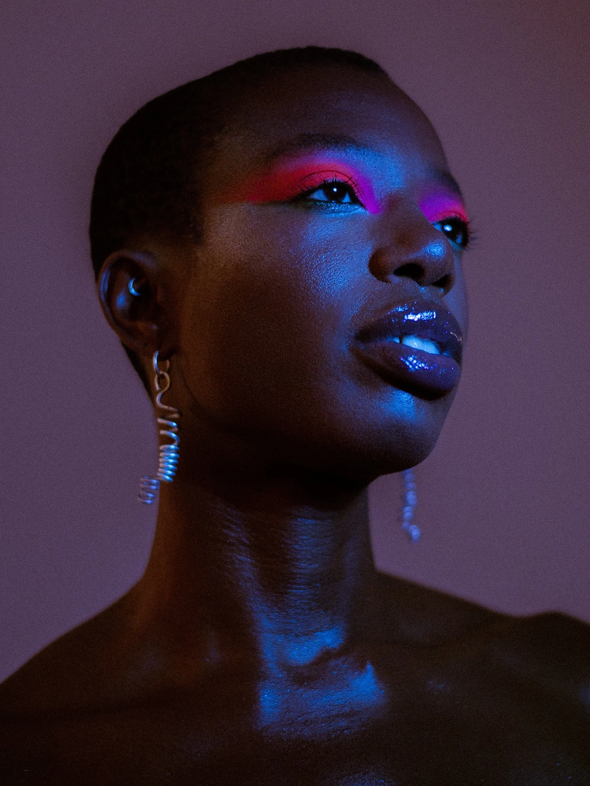 Close-up portrait of a woman with dark skin and short hair, wearing vibrant eye makeup and glossy dark lipstick, against a dark background, A woman with curly black hair wearing bright makeup, earrings, a rainbow beaded bracelet, and a necklace with 