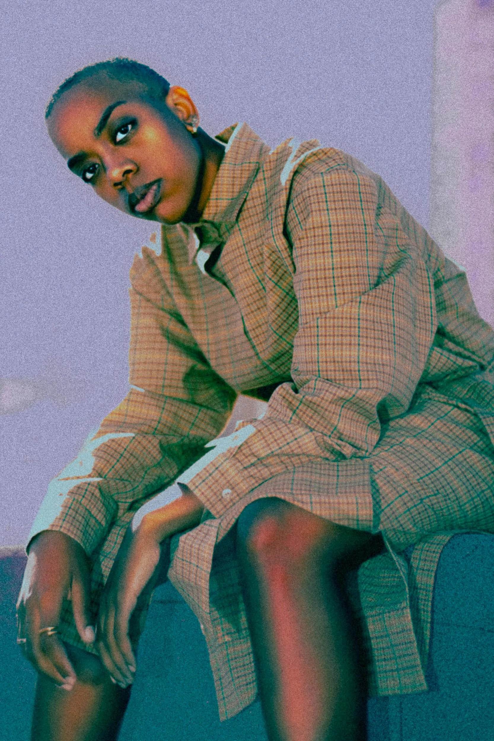 A person with short hair and earrings sitting on a blue sofa, wearing a beige plaid suit, looking at the camera, photographed during a photography session in California for a portrait editorial with fashion photographer.