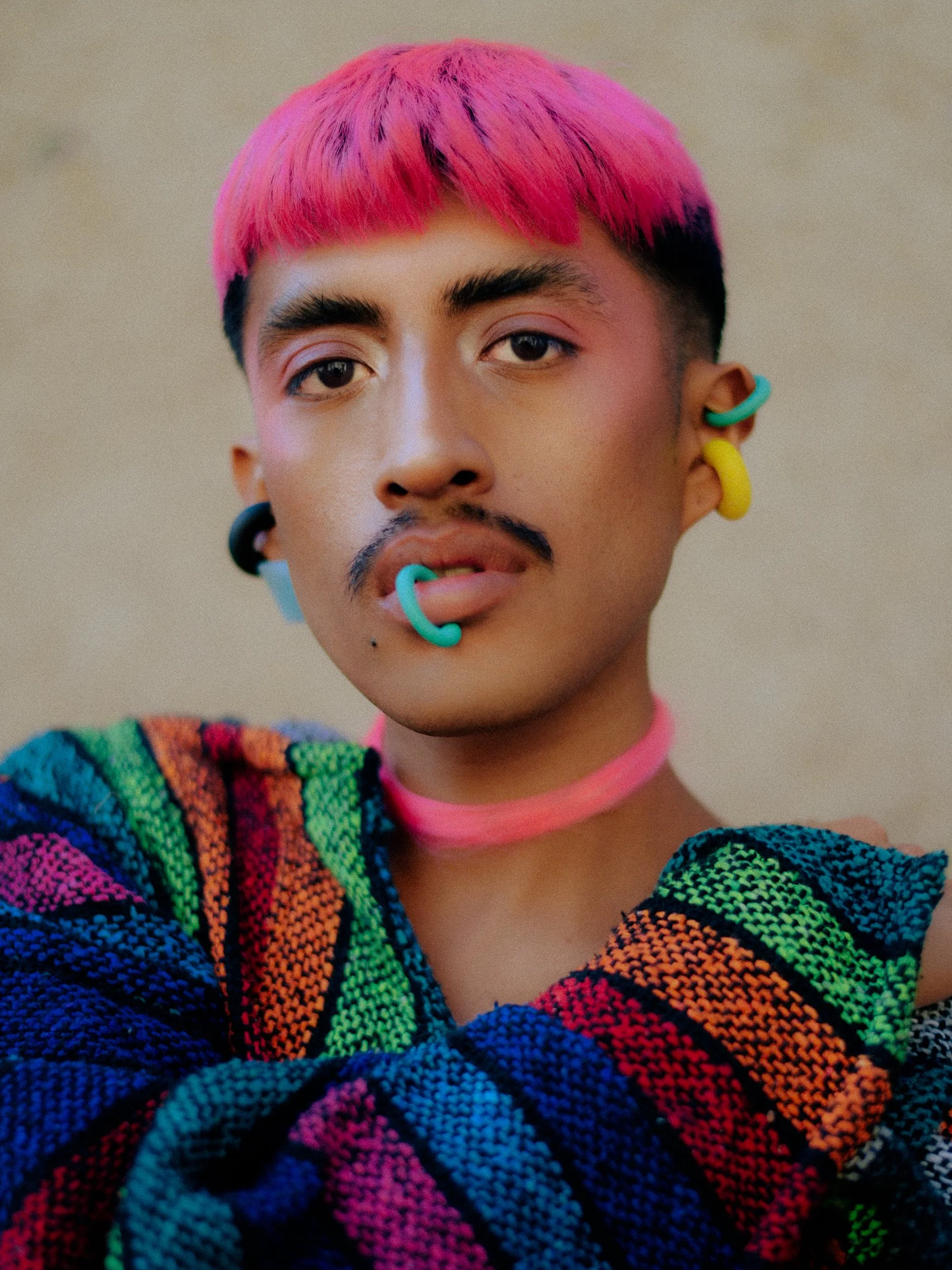 Close-up portrait of a feminine model  with pink and black hair, colorful accessories including earrings and a choker, and wearing a rainbow-colored knitted sweater, photographed during a fashion editorial photography session in Los Angeles with fash
