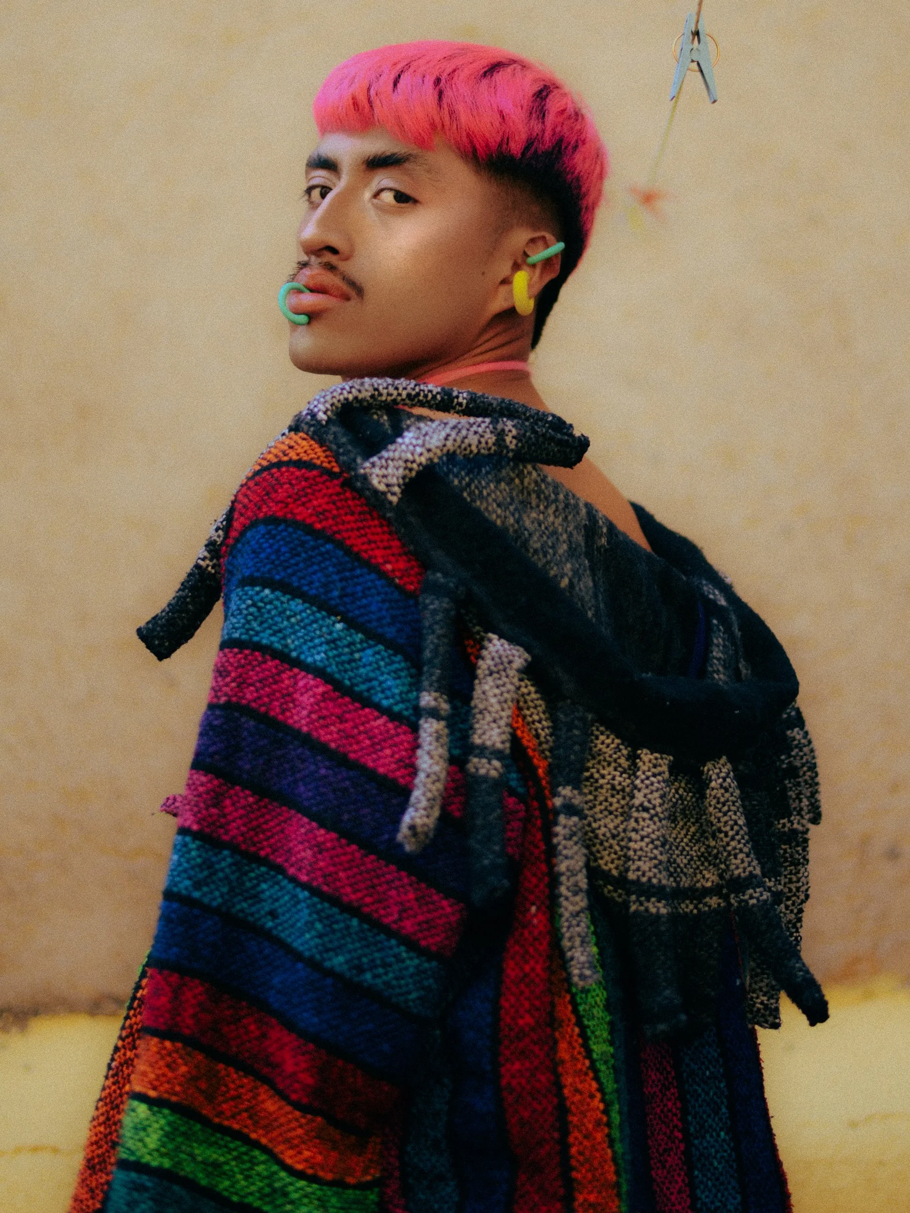 A feminine person model with pink hair, multiple facial piercings, and colorful clothing posing indoors, photographed during a fashion editorial photography session in Los Angeles with fashion photographer Gí Tenamá.