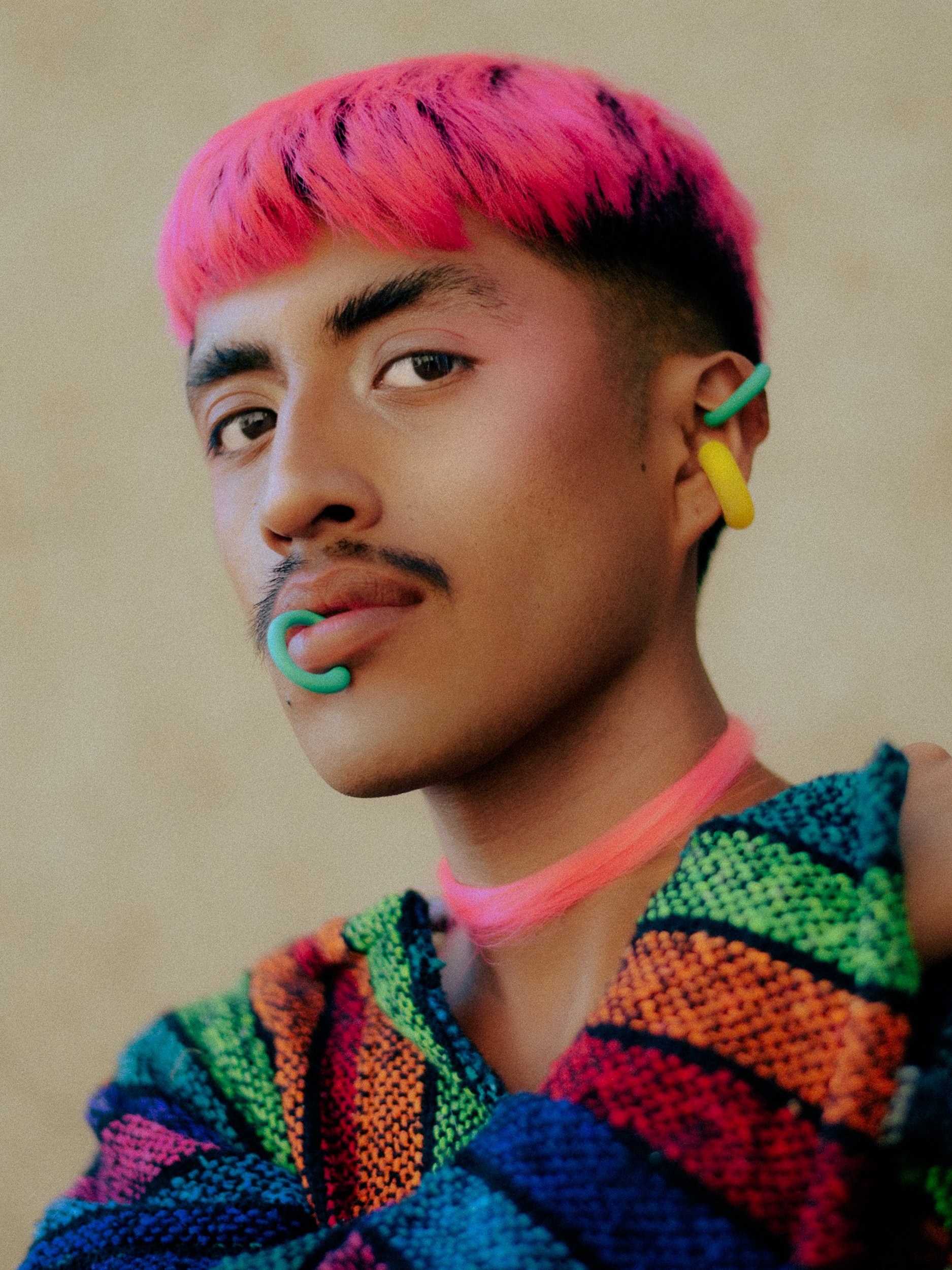 A feminine model with short pink hair, colorful earrings, and rainbow-patterned sweater, looking at the camera, photographed during a fashion editorial photography session in Los Angeles with fashion photographer Gí Tenamá...