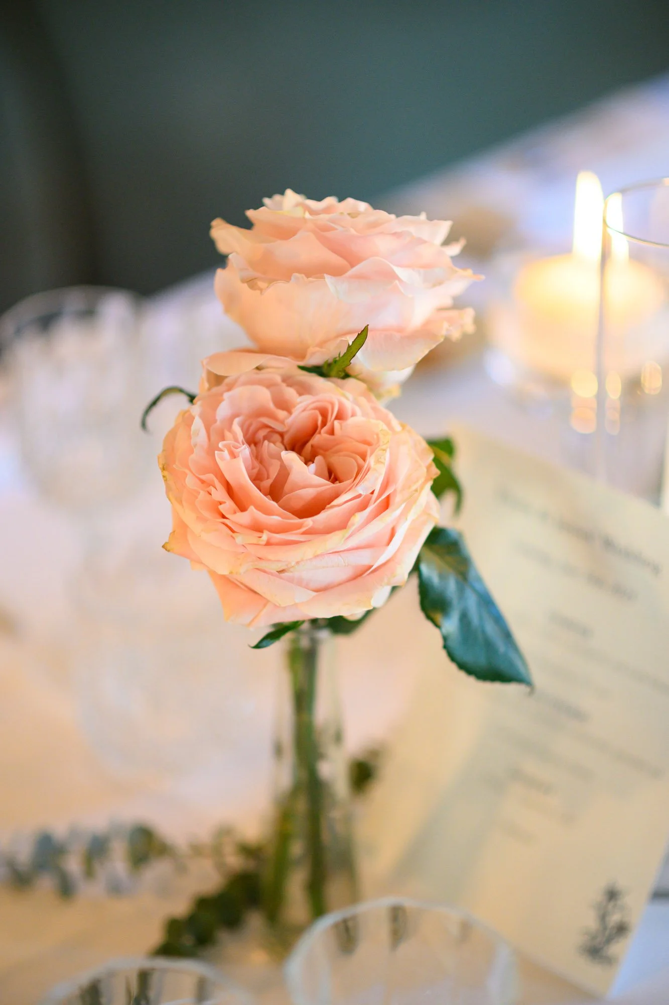 Fleurs roses dans un vase sur une table décorée, avec des bougies allumées en arrière-plan.