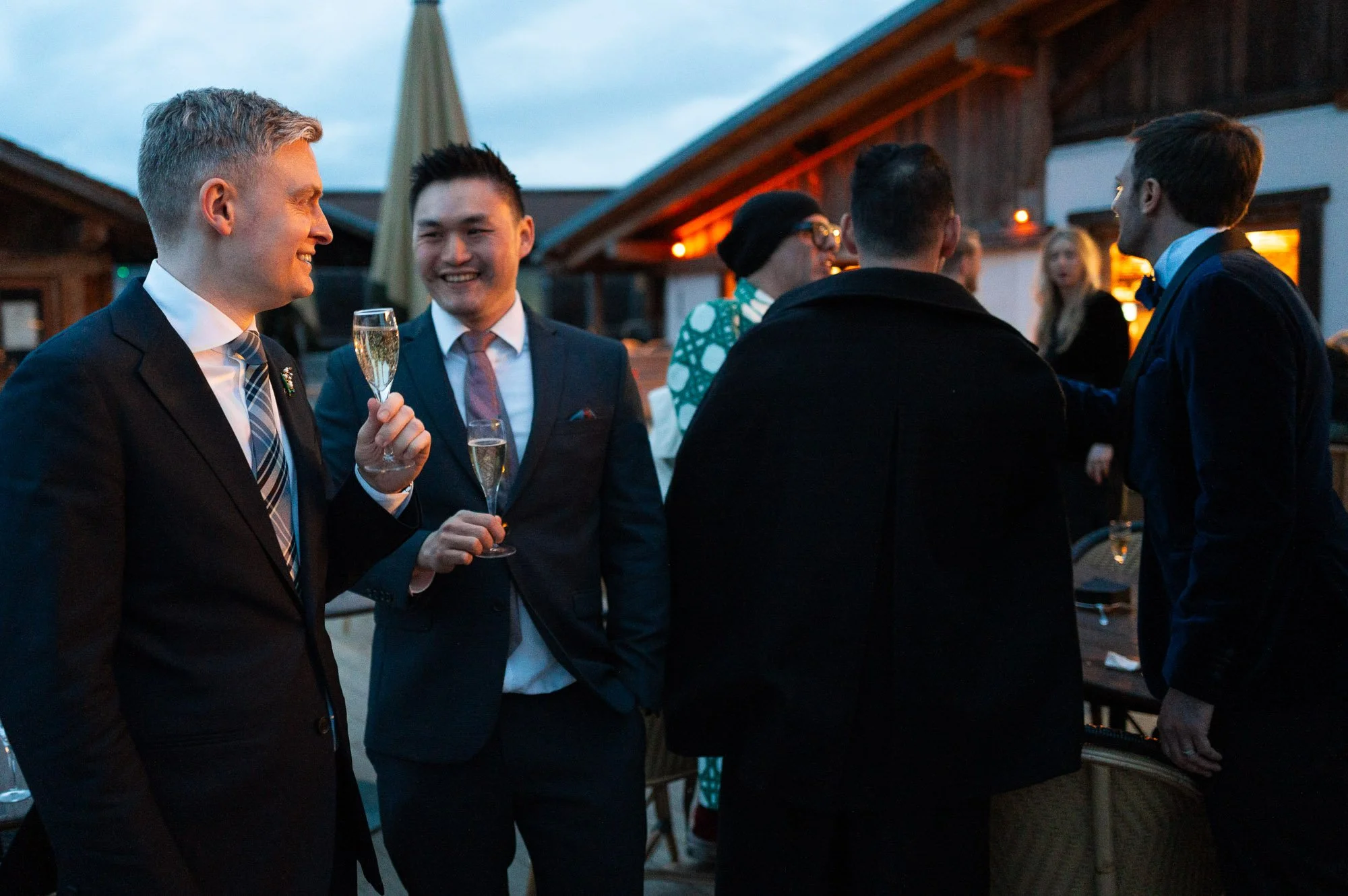 Groupe de personnes en costume social à une fête en extérieur avec boissons, ambiance chaleureuse et éclairage d'ambiance.