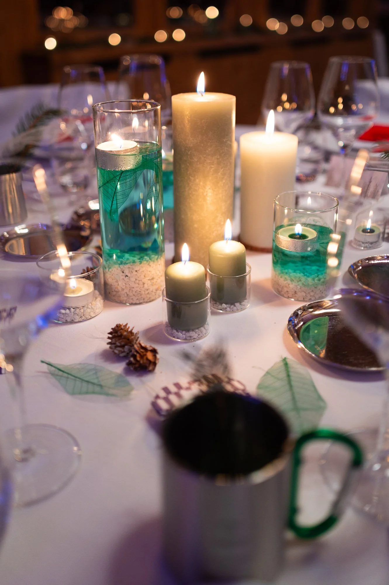 Table de fête décorée avec des bougies, des verre à vin, une tasse, et des feuilles décoratives.