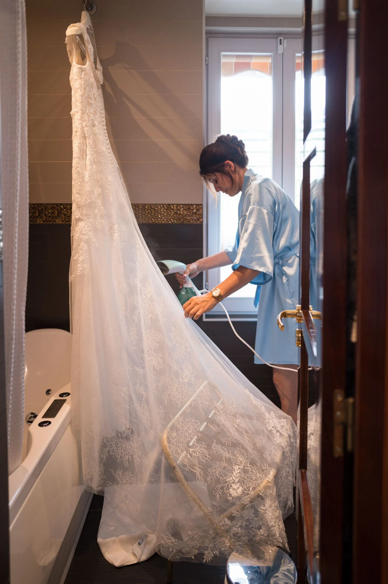 Femme utilisant un fer à repasser le train d'une robe de mariage dans une salle de bain