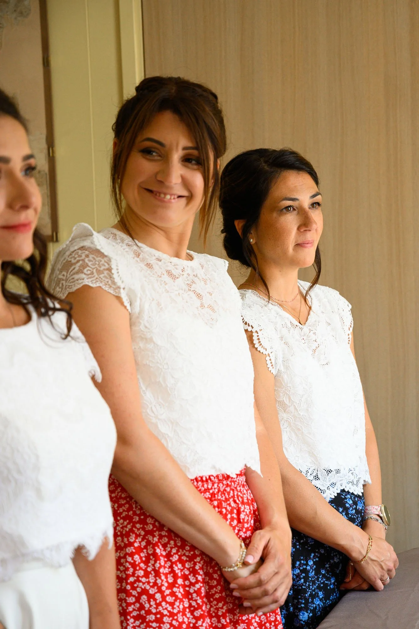 Trois femmes en vêtements blancs en train de prendre la pose, souriantes et sérieuses, dans une pièce intérieure.