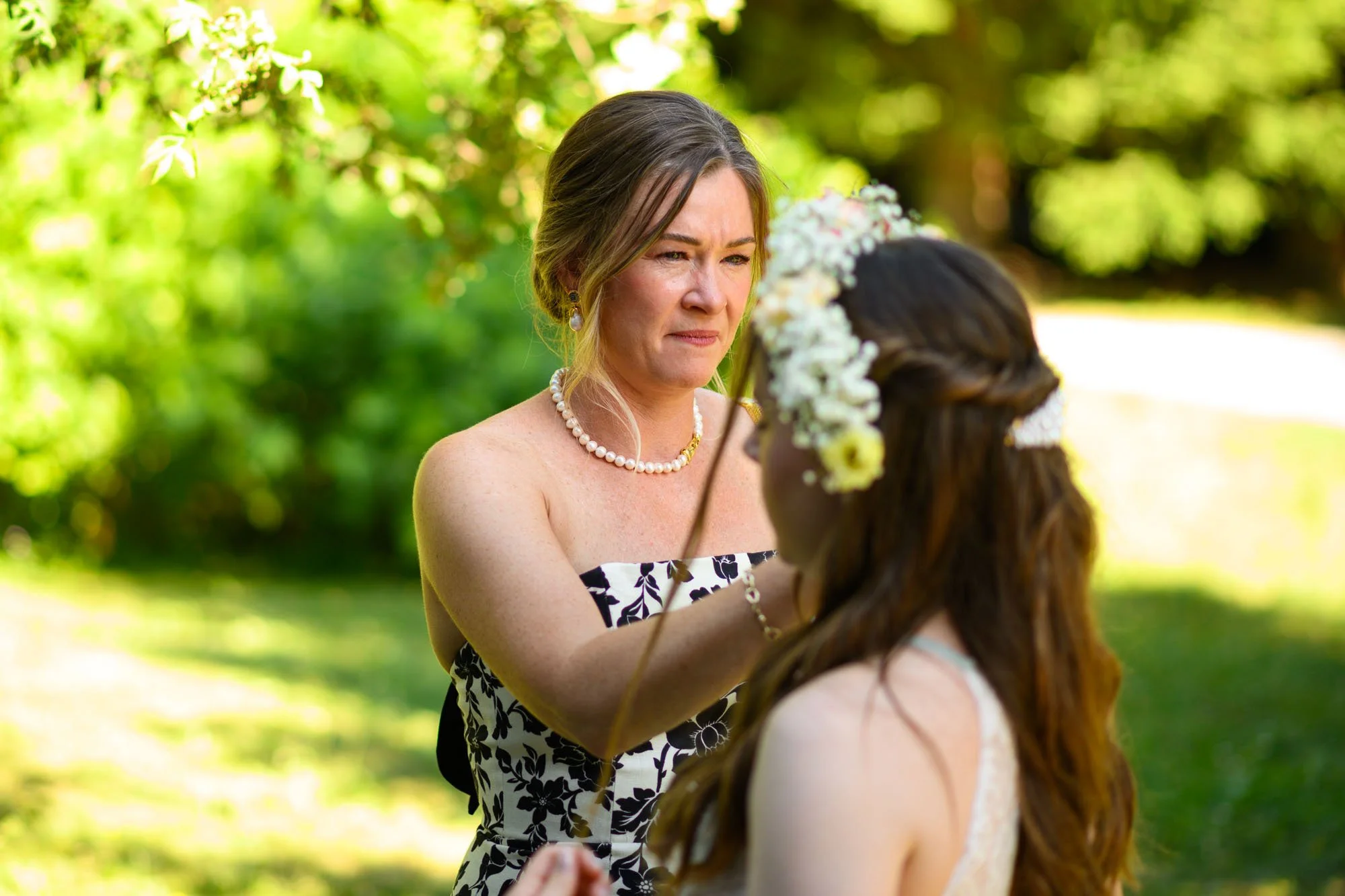 Une femme en robe de cérémonie orne la main de jeunes fille lors d'une cérémonie en plein air.