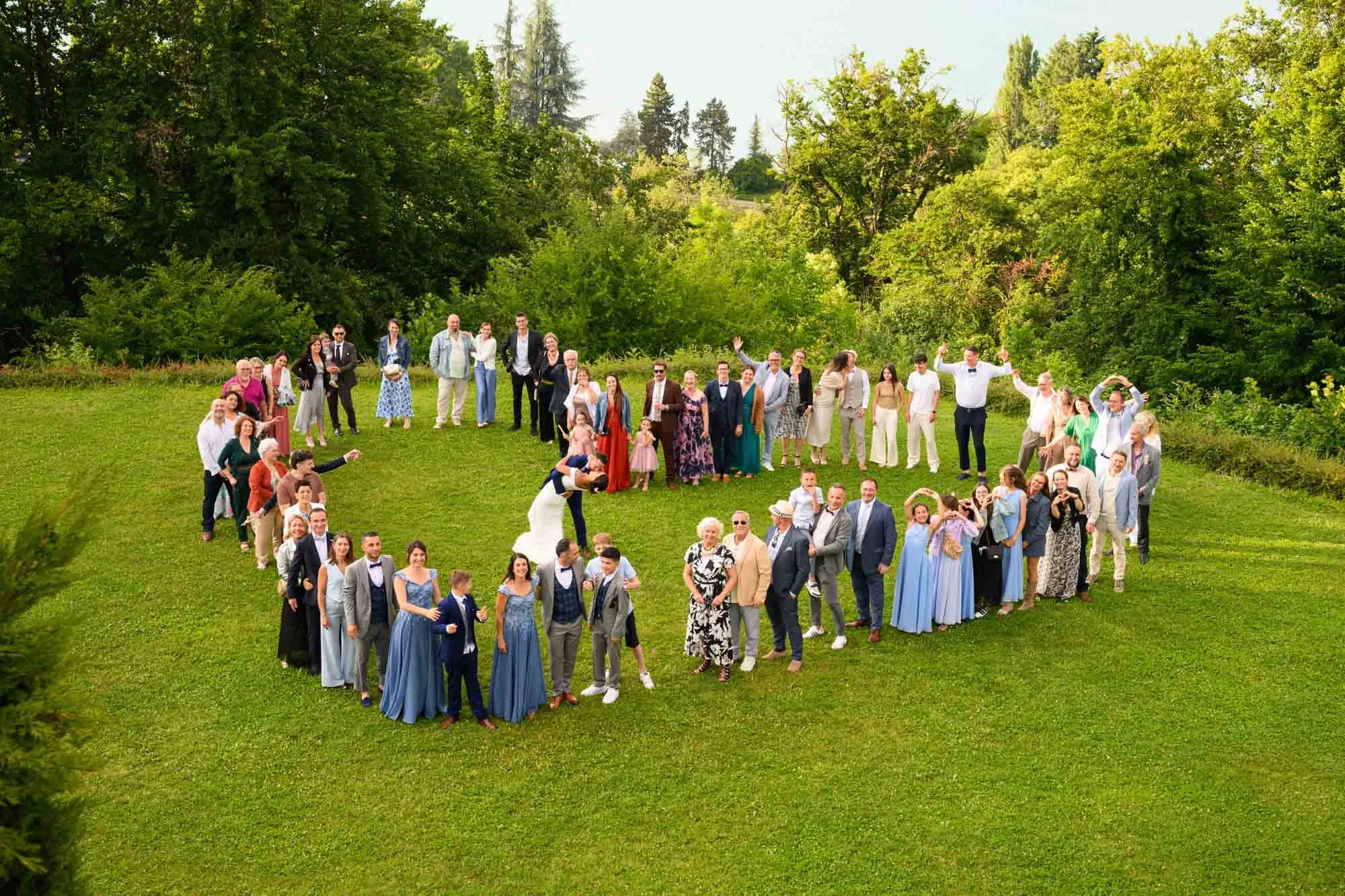 Groupe de personnes formant un cœur sur une pelouse verte avec des arbres en arrière-plan, lors d'un événement en plein air.
