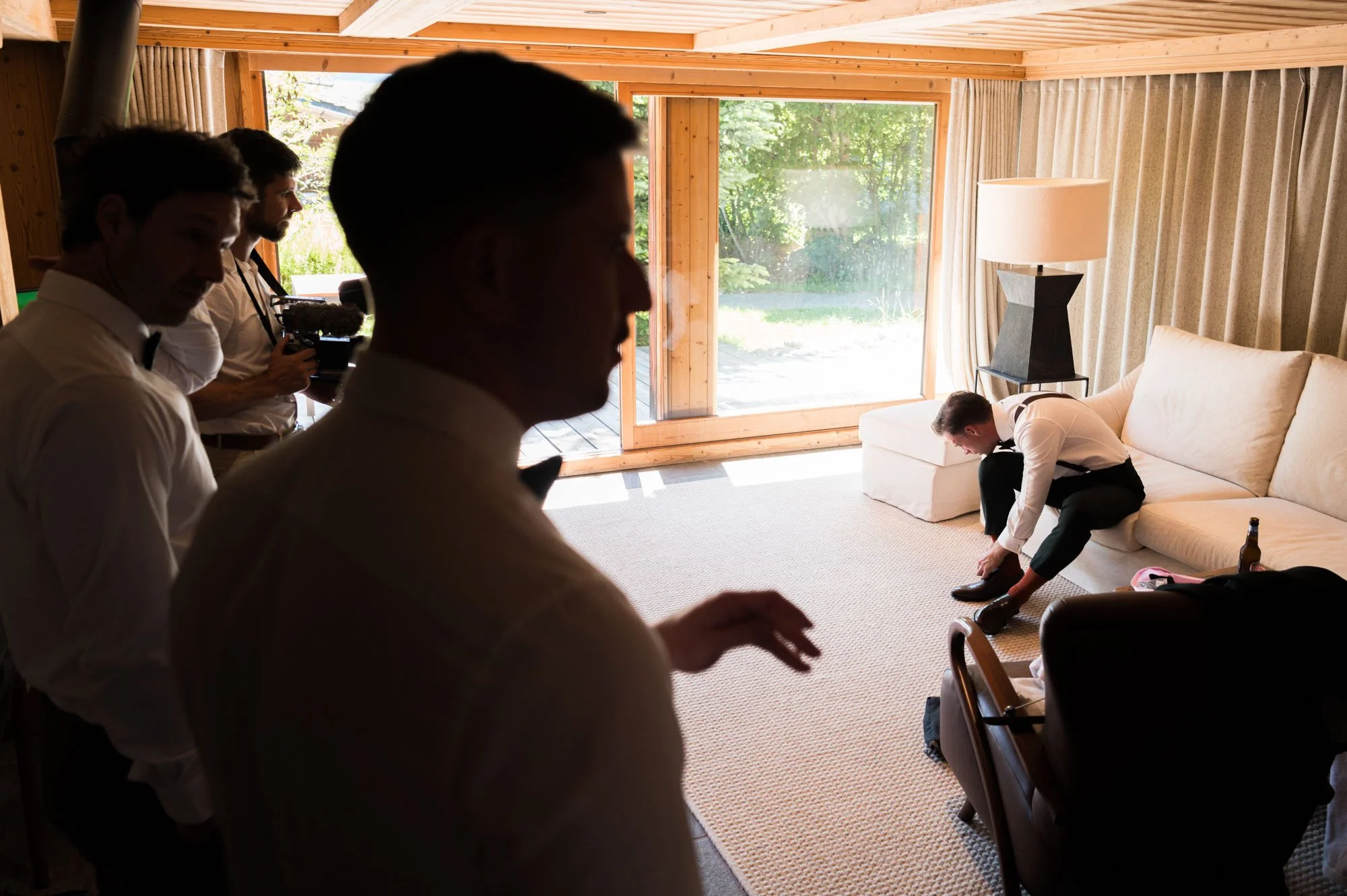 Un groupe d'hommes en costume se prépare pour une séance photo ou vidéo dans un salon lumineux avec de grandes fenêtres donnant sur un jardin.