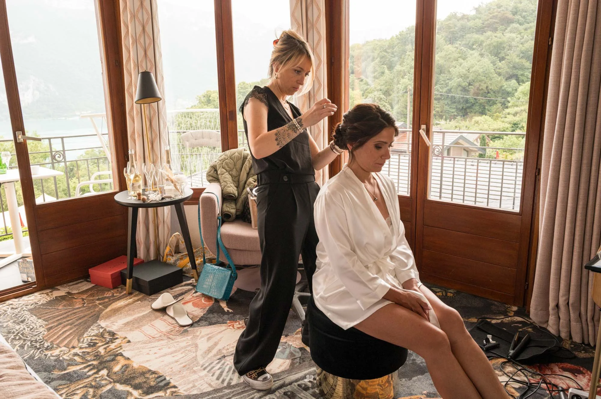 Femme recevant une coiffure par un styliste dans une pièce lumineuse avec une vue sur la nature.