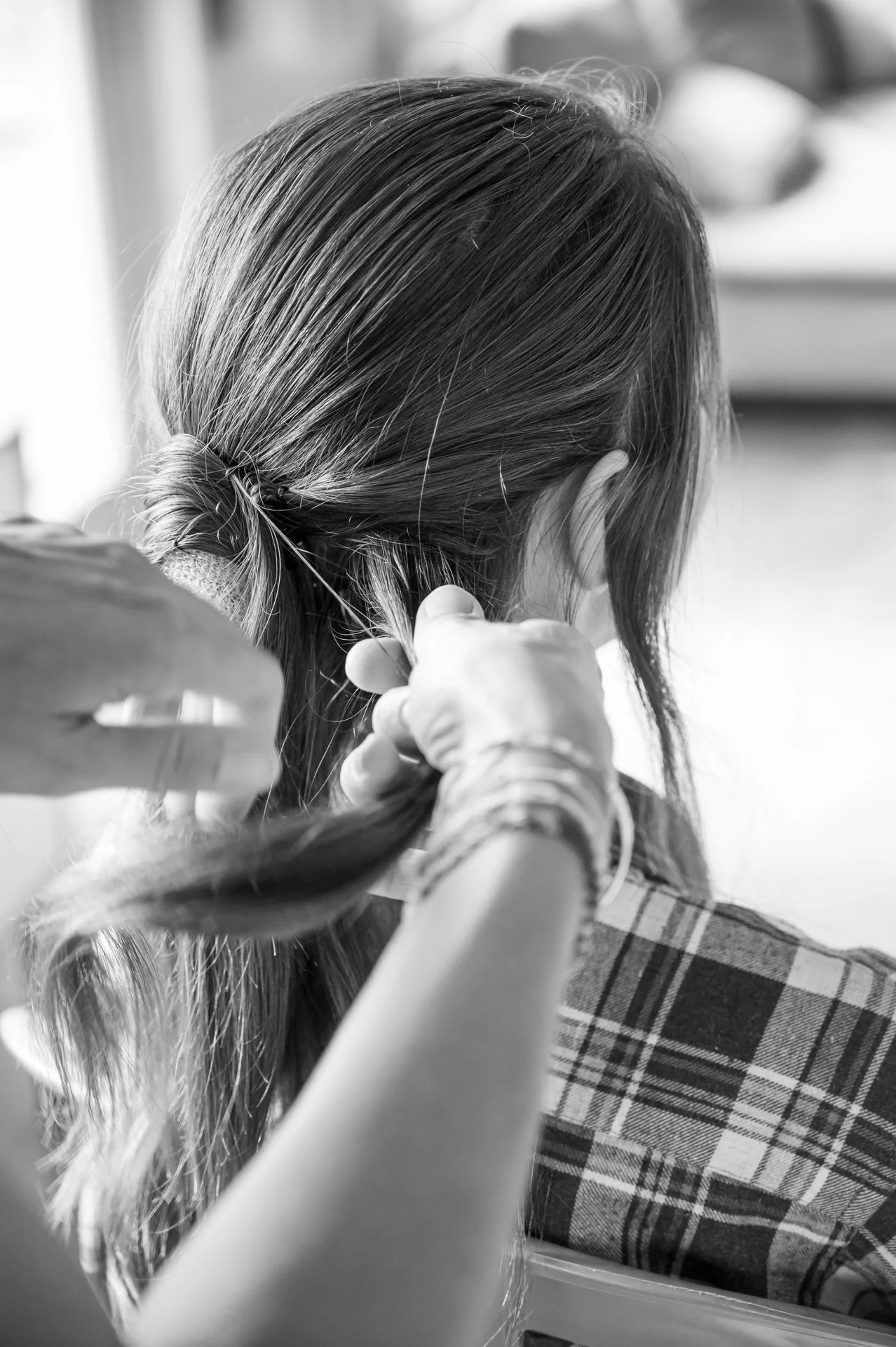 Une personne coiffe une femme avec un elastique, vue de dos, en noir et blanc.