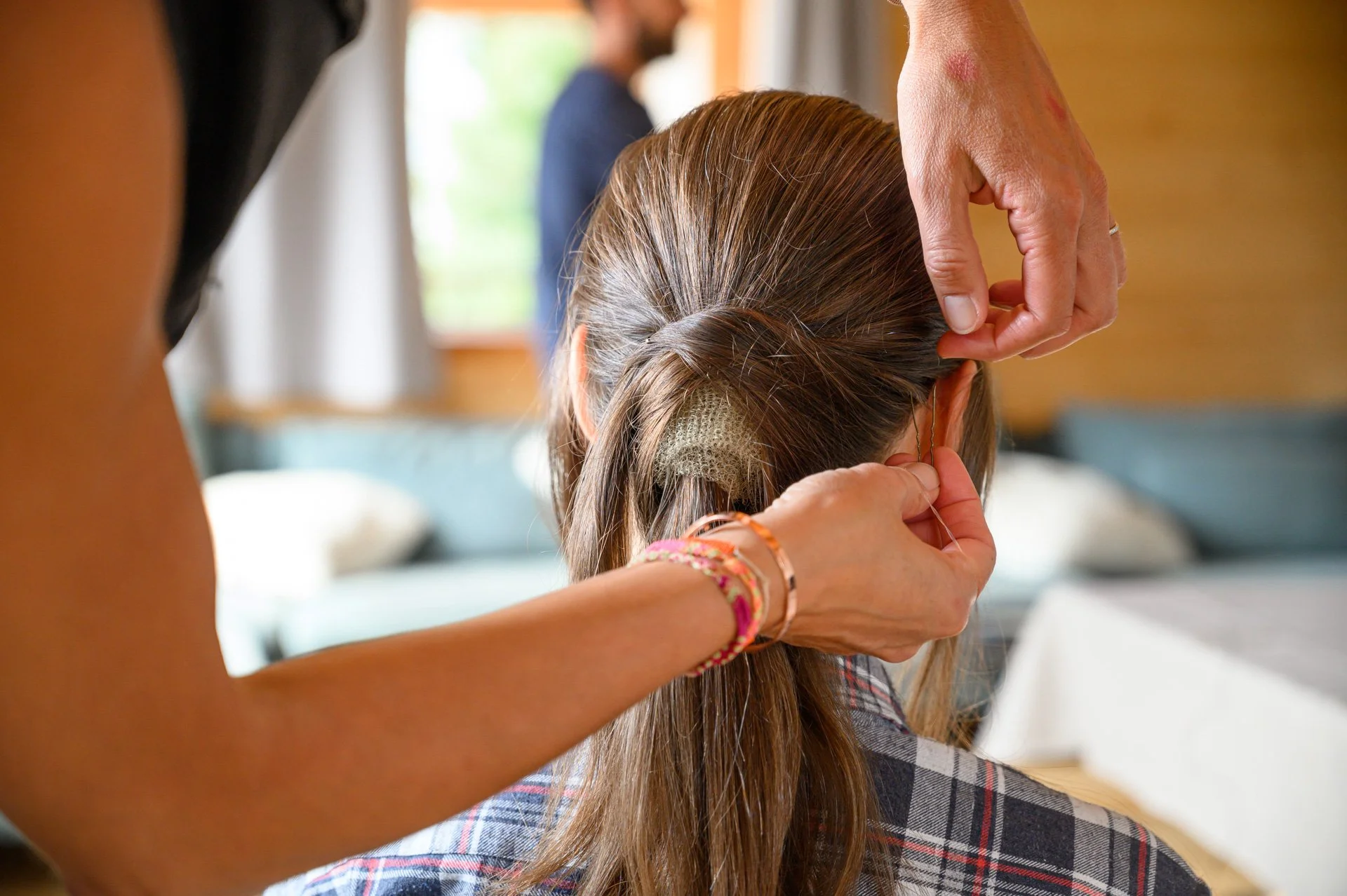 Une personne regarde une autre personne se faire tresser les cheveux, située en intérieur.