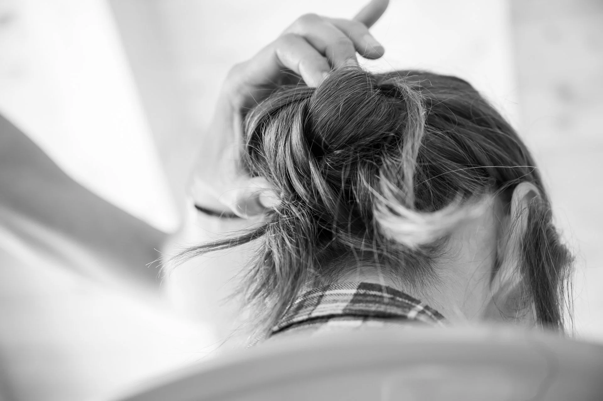 Une personne coiffant ou manipulant les cheveux d'une autre personne, vue de dos, en noir et blanc.