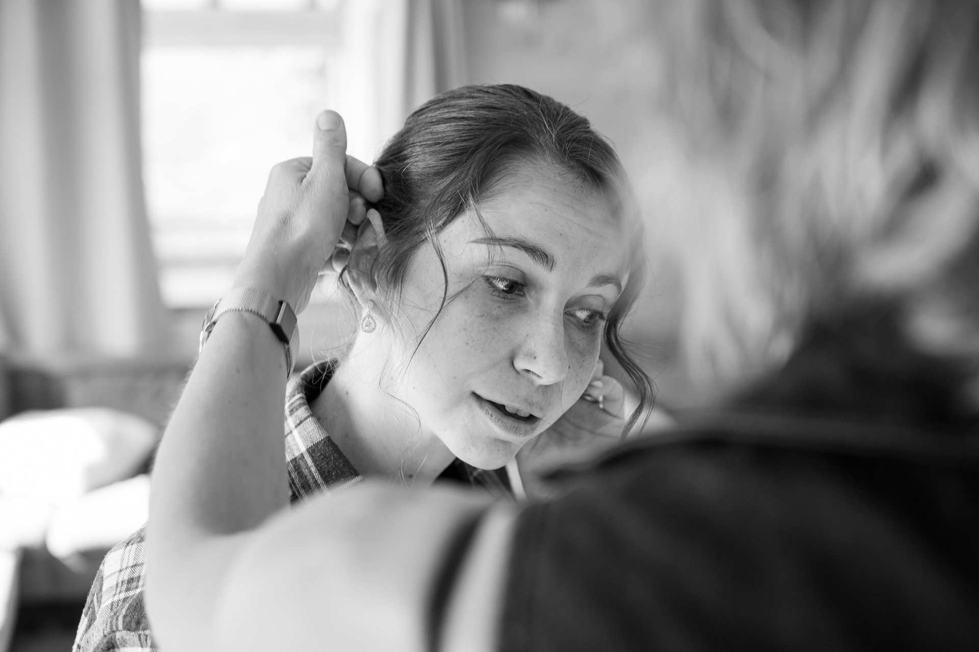 Jeune femme avec des taches de rousseur, se faisant coiffer par une autre personne, dans un intérieur.
