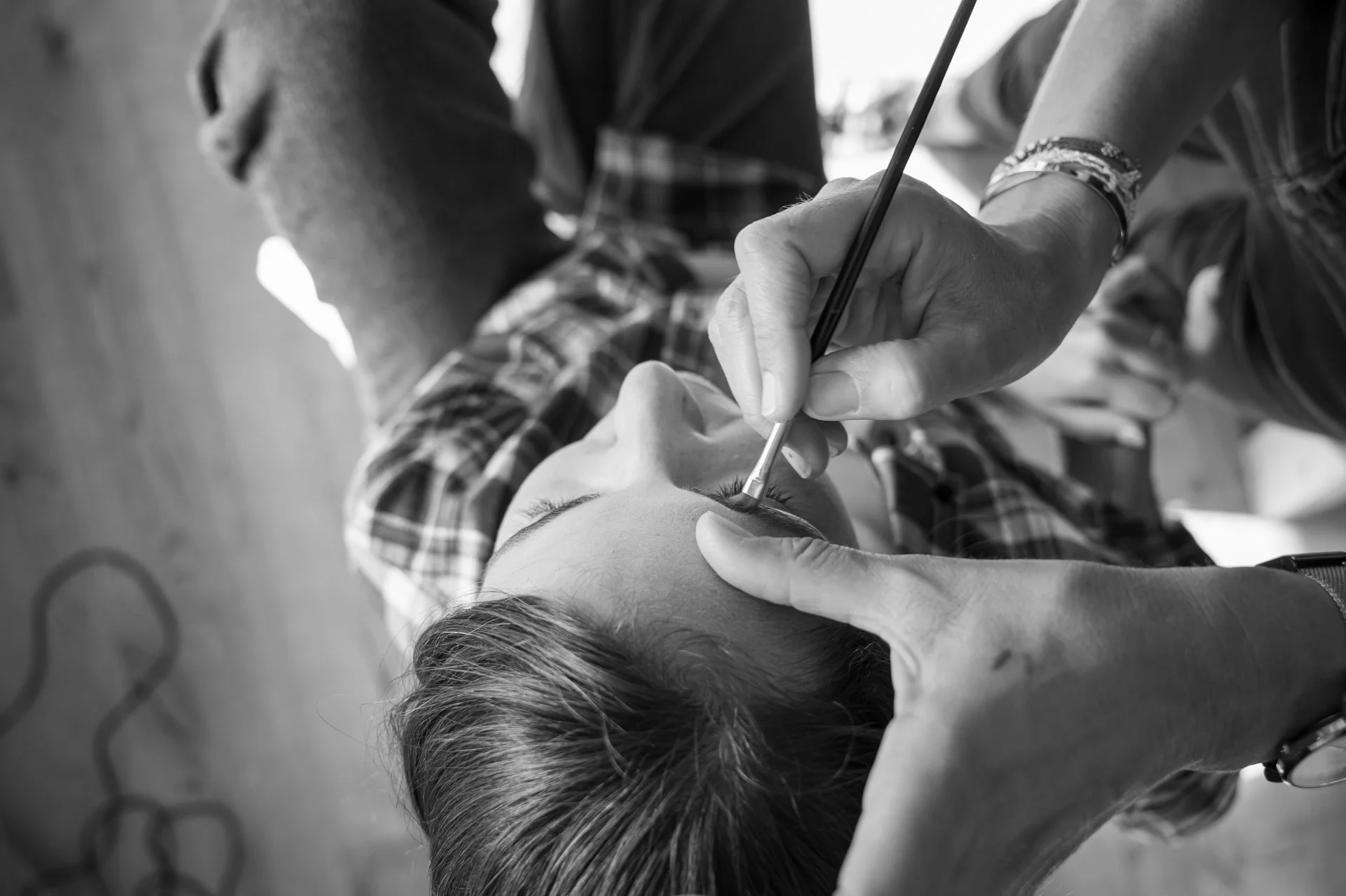 Une femme en train de se faire maquiller les yeux par une professionnelle, dans un environnement intérieur.