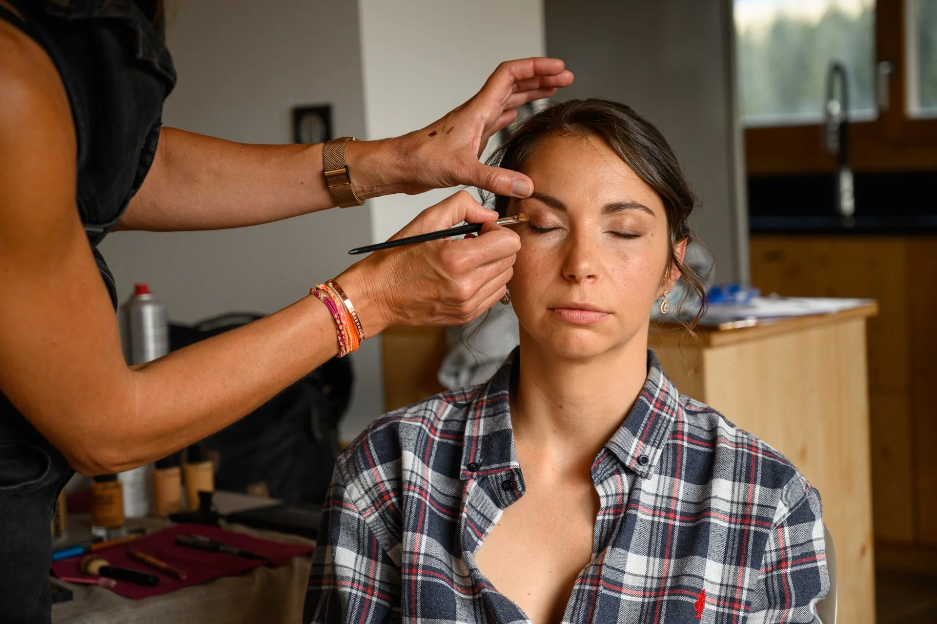 Une femme se fait maquiller par une artiste maquilleuse dans un intérieur.