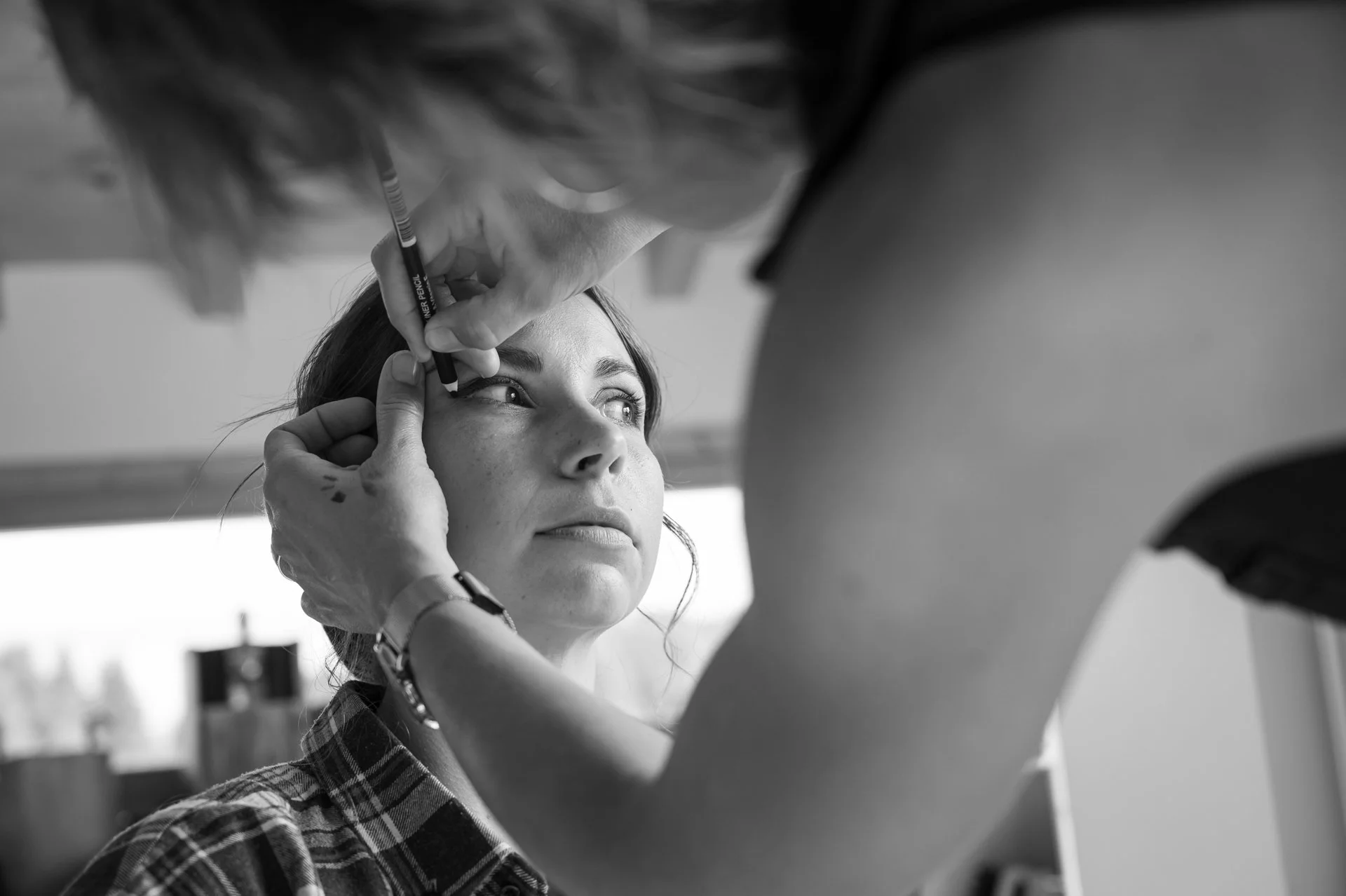 Une femme se fait maquiller par un artiste en maquillage, vue en gros plan en noir et blanc.