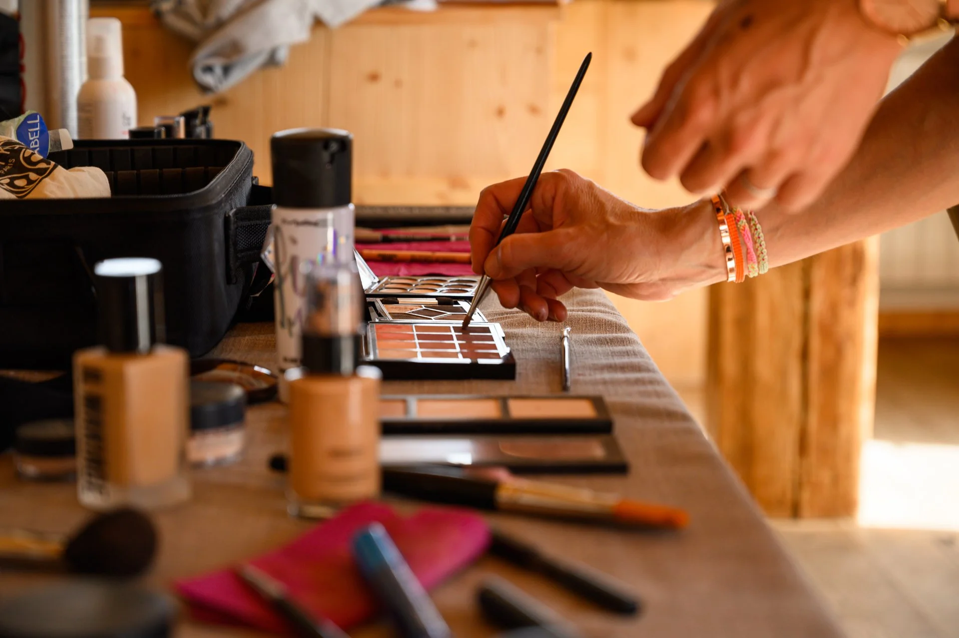 Personne appliquant du maquillage avec des pinceaux et des palettes de maquillage sur une table en bois.