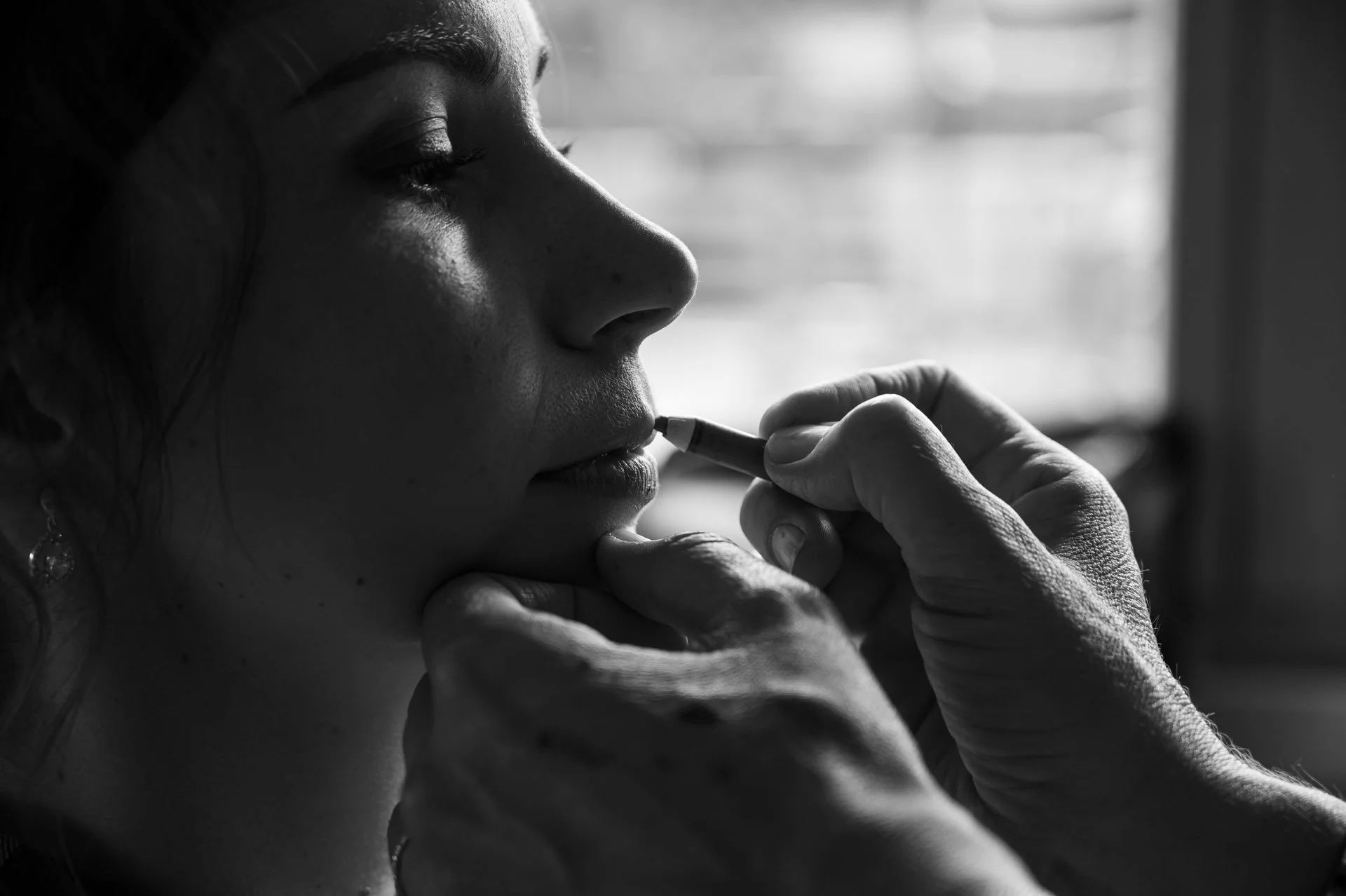 Une femme est en train de se faire maquiller les lèvres par une autre personne. L'image est en noir et blanc.