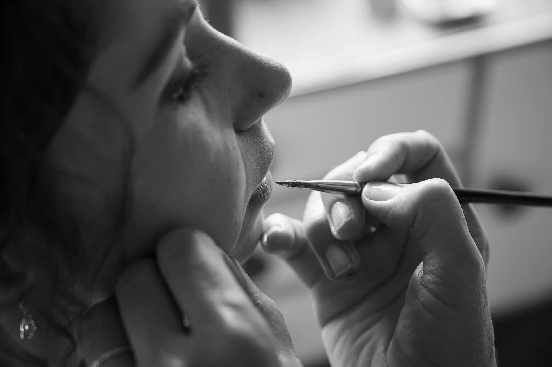 Une personne maquille les lèvres d'une autre personne, en utilisant un pinceau pour appliquer du maquillage.