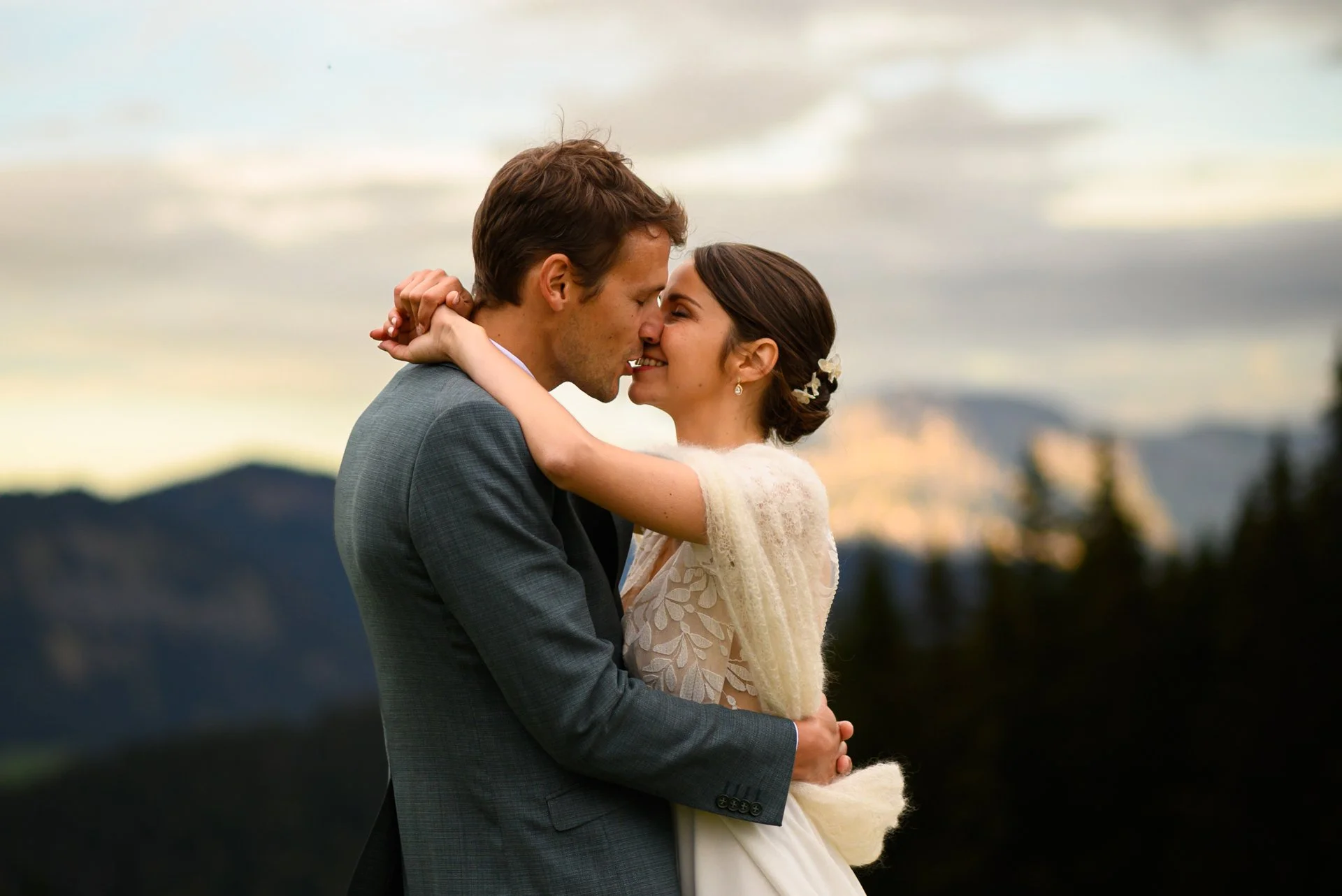 Un couple danse lors de leur mariage à l'extérieur, avec une montagne en arrière-plan, pendant un coucher de soleil.