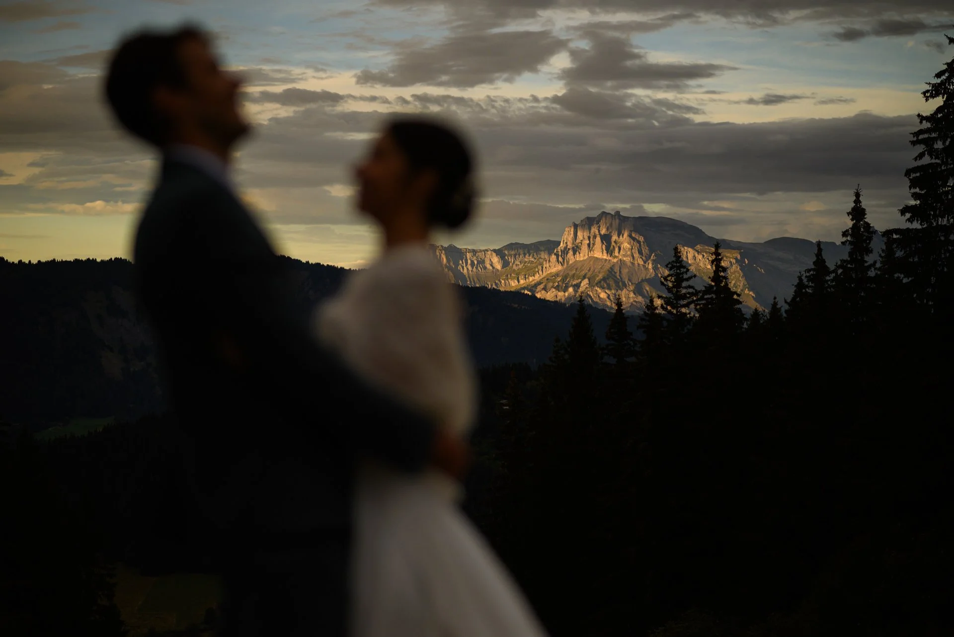 Silhouette d'un couple habillé en mariés devant un paysage de montagnes au coucher du soleil.