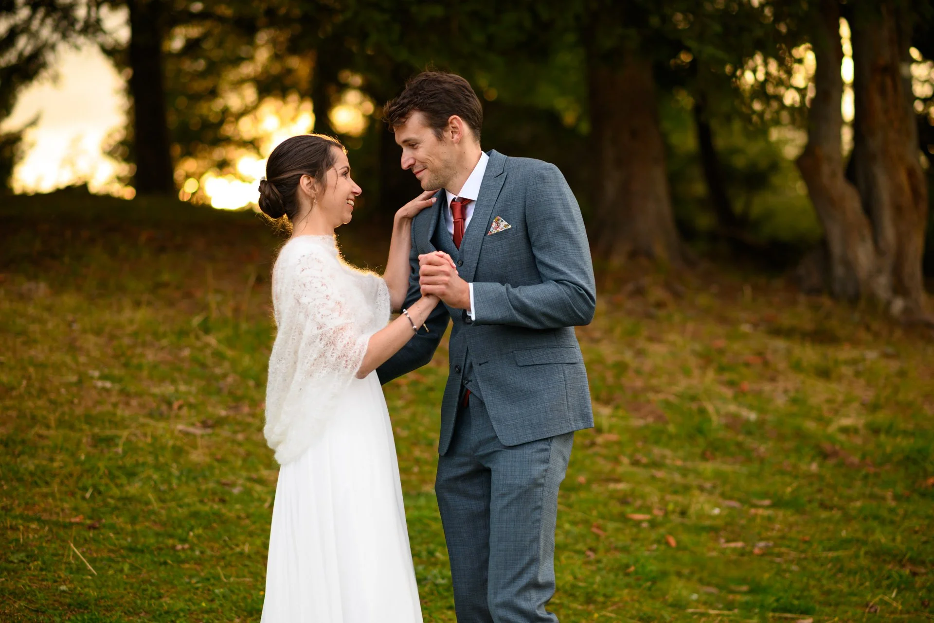 Un couple en tenue de mariage danse dans un parc lors d'un coucher de soleil, entouré d'arbres.
