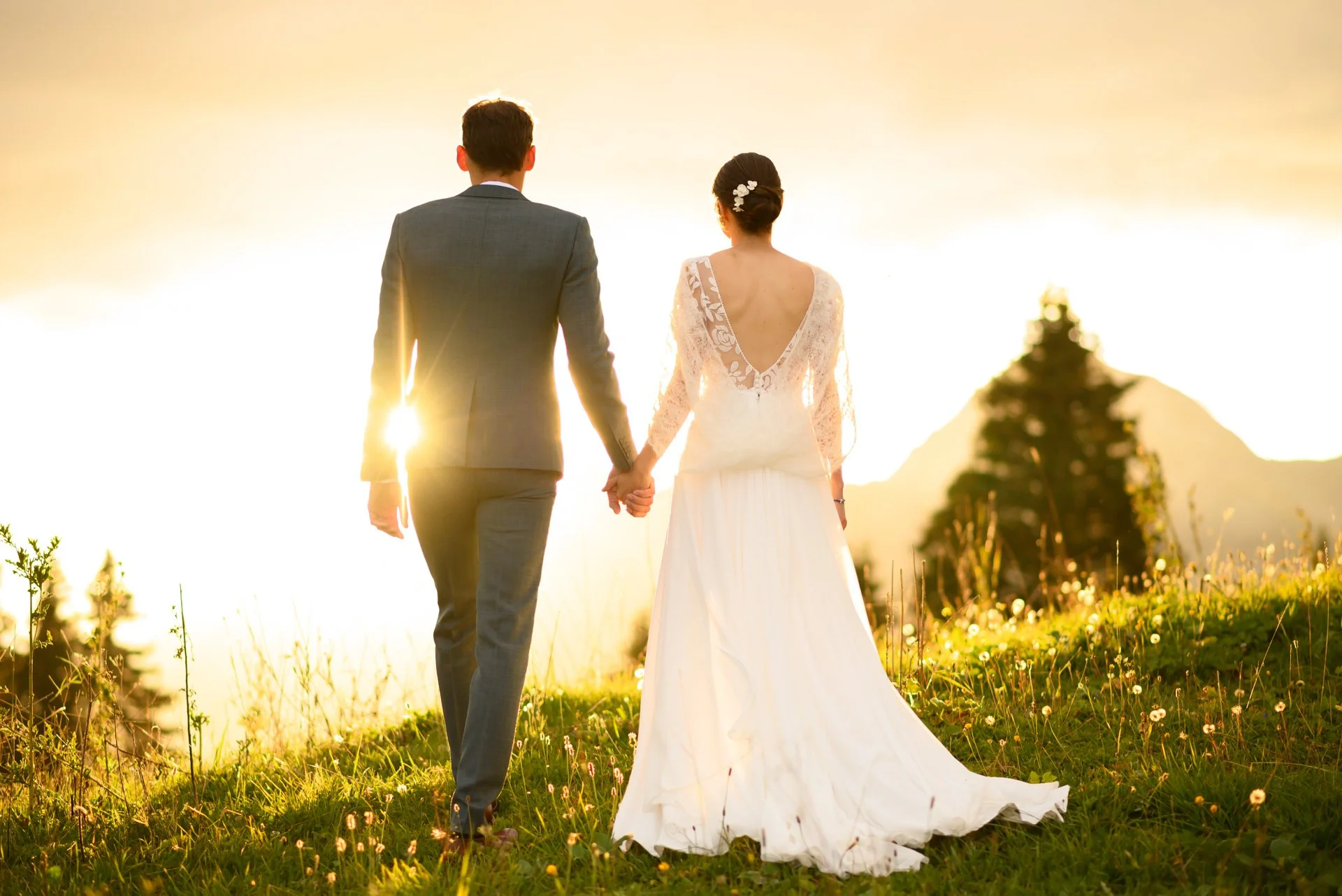 Un couple de mariés marche main dans la main dans un champ lors d'un coucher de soleil.