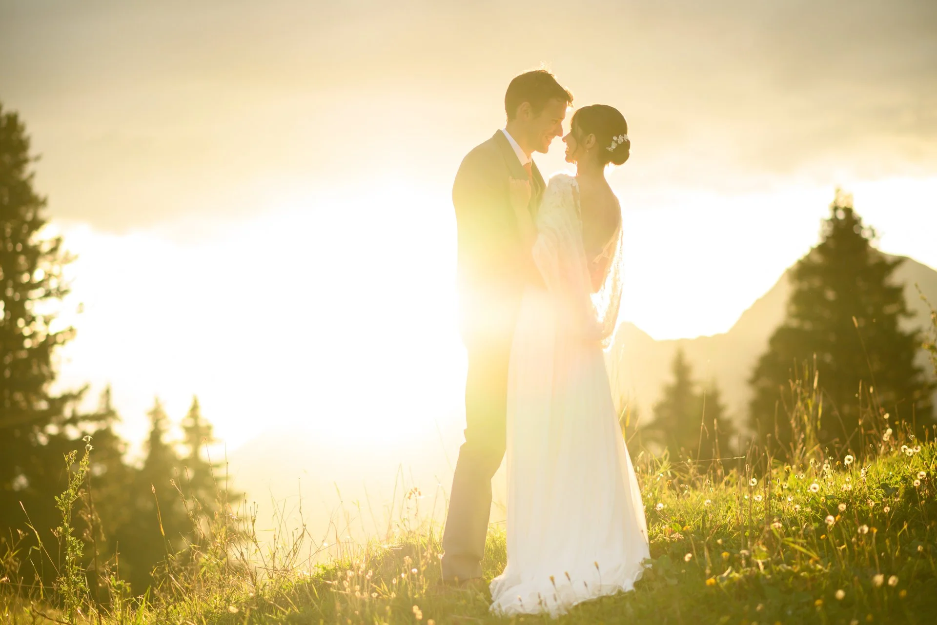 Un couple en mariage se tient dans un champ avec la lumière du soleil couchant en arrière-plan.