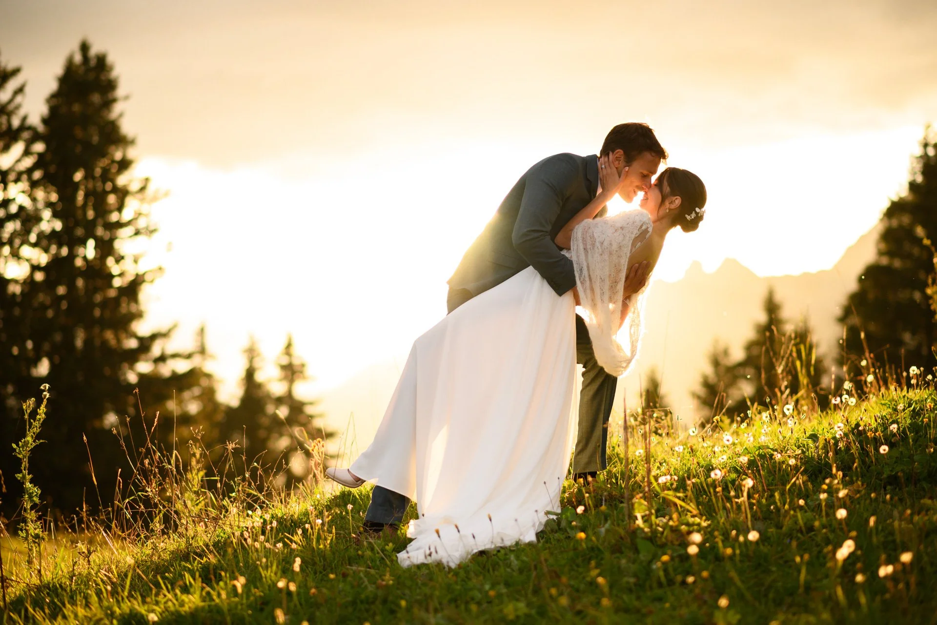 Un couple de mariés danse dans un champ lors d'un coucher de soleil, avec des arbres en arrière-plan.
